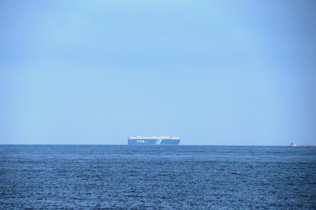 かすんだ水色の空と、青い海。そのあいだの水平線だけがくっきりと一本通っていて、その線の上に、白と青の大きな船が一隻、小さく乗っている。右の端には、赤い小さな船も見える。