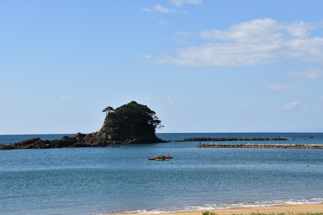 あづり浜の沖に浮かぶ松の小島と、そばを進む赤と黄色のカヤック