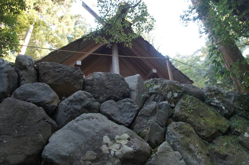 苔の生えた大きな石が積まれた石垣。その上に小さな社の屋根が見える