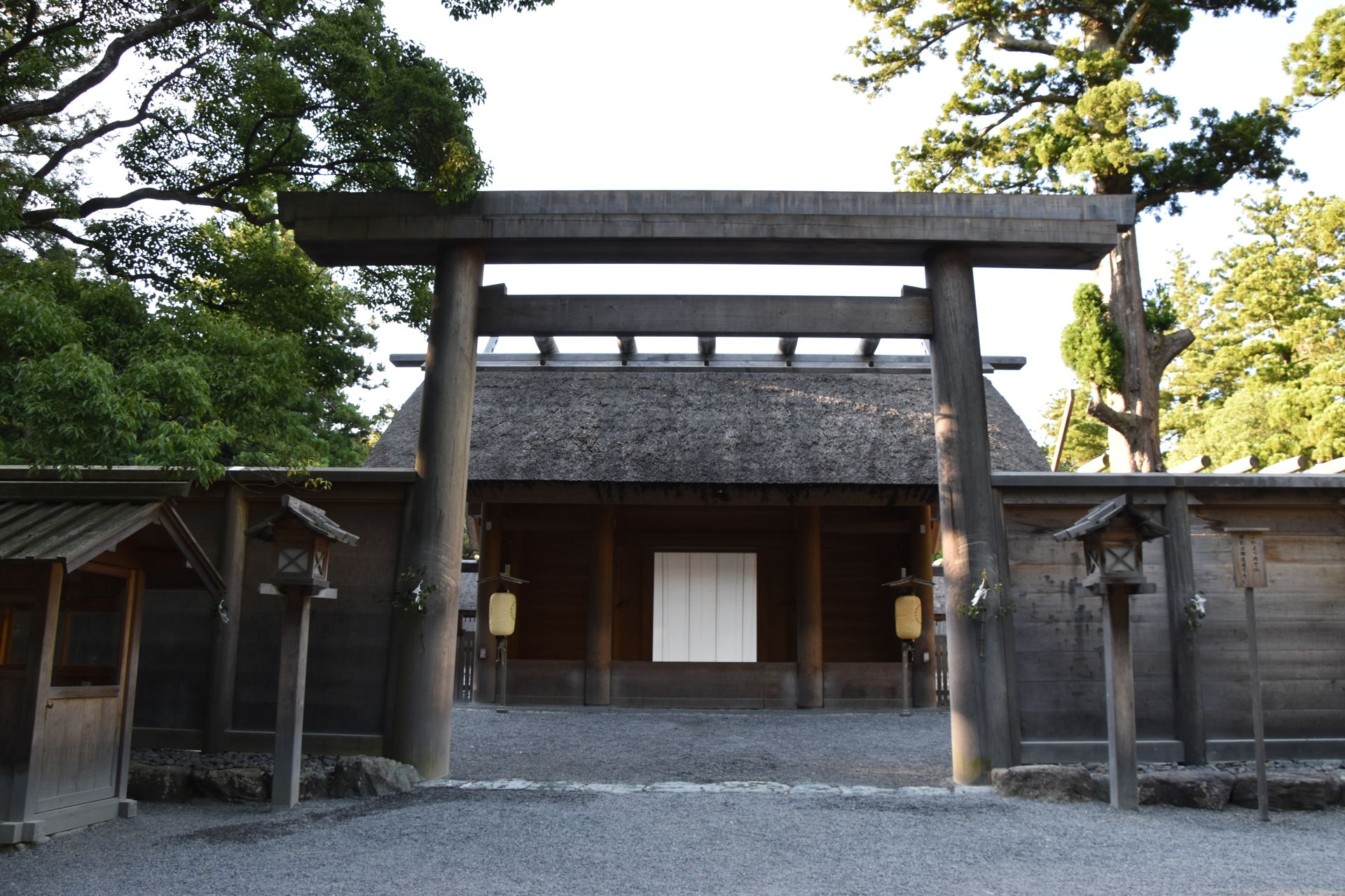 夕方の正宮の門。木々の緑に囲まれ、門の前の砂利に長い影がある