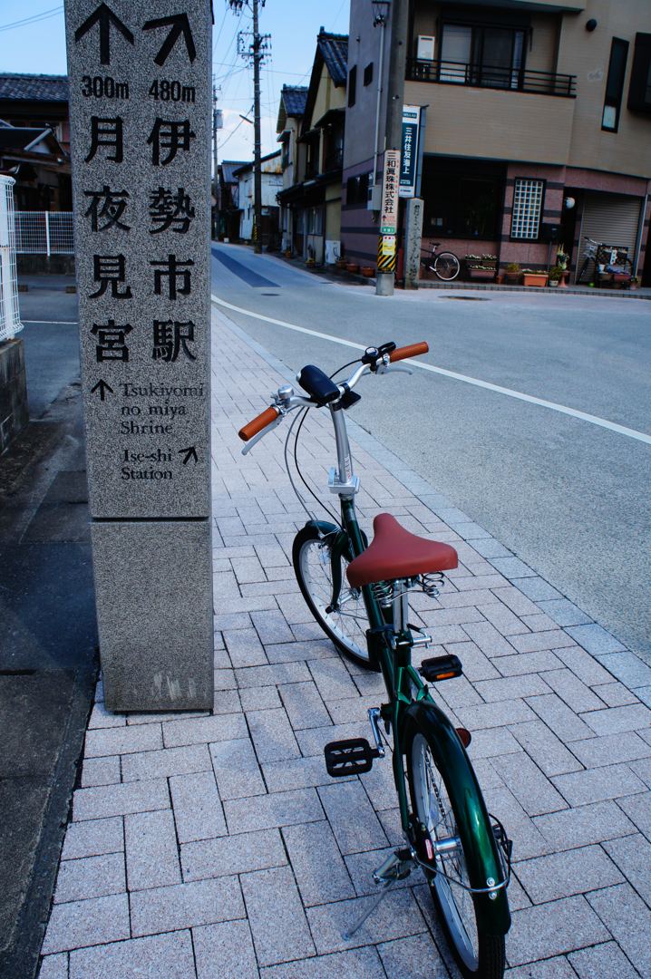 道ばたの石の道しるべ。「月夜見宮」「伊勢市駅」と刻まれ、手前に自転車が停めてある